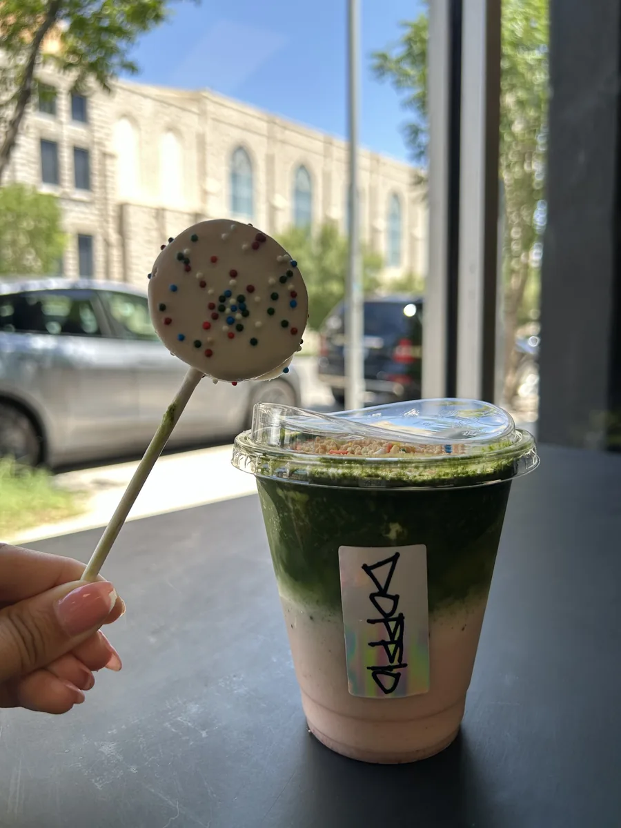 Layered iced matcha over strawberry in a Doppio cup, with a sprinkle cake pop, by the window on Montana Ave