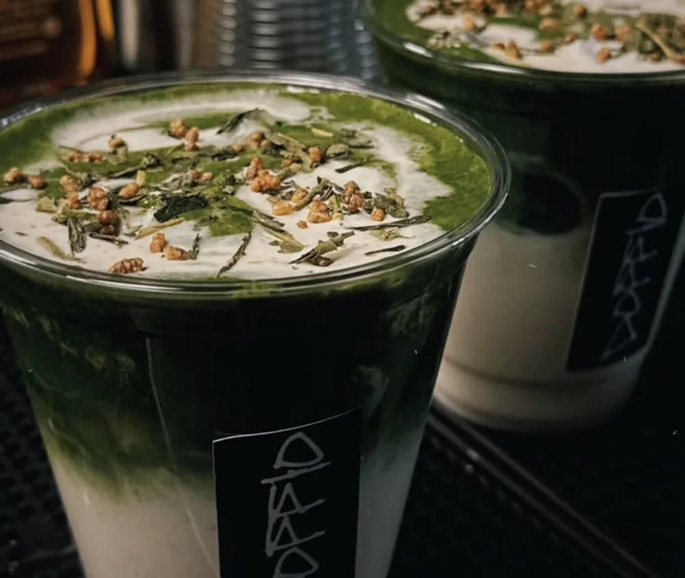 Two layered matcha lattes topped with toasted rice and tea leaves