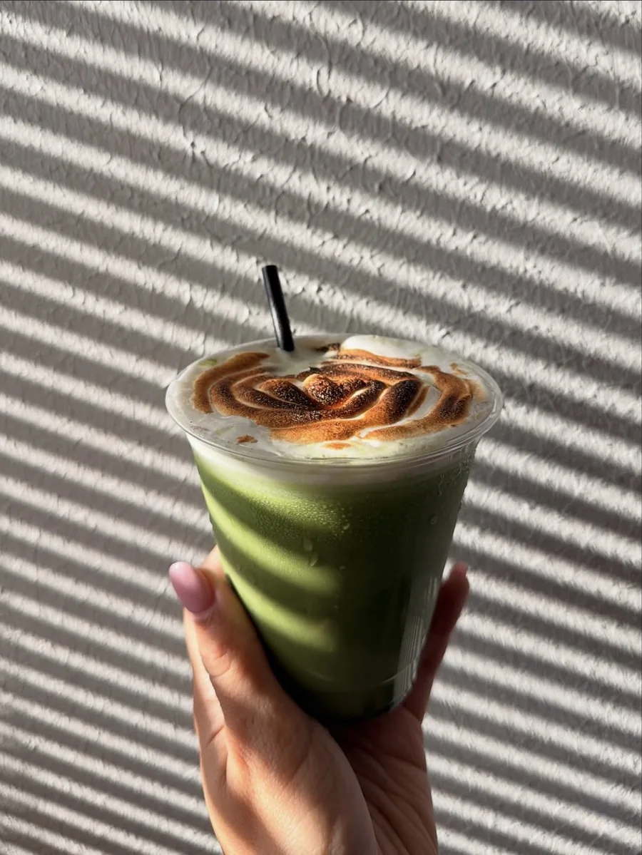 Iced Kettl matcha with a torched topping, held up against striped window light