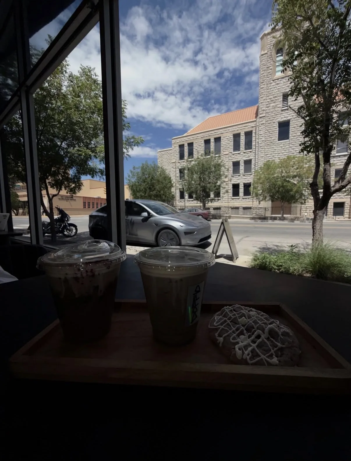 View from a window table at Doppio onto Montana Ave, with two iced drinks and a cookie on a tray