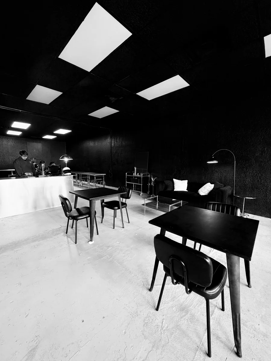 The Doppio room: black walls, ceiling light panels, tables, a lounge sofa and the stainless bar
